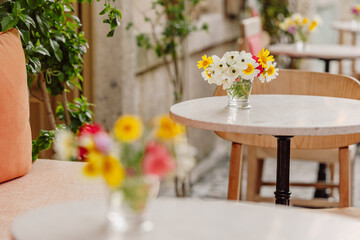 Small glass vase containing a colorful bouquet of wildflowers decorating a table in a restaurant with an out of focus background