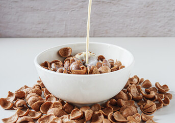 Chocolate corn flakes Cereal with pouring milk on white background
