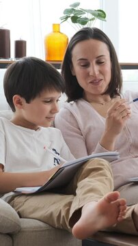 Happy mother and son learning together, completing schoolwork and exercise at home, engaging in education with joy in a supportive environment. Vertical video.