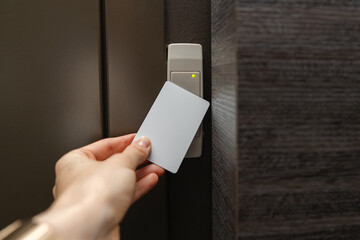 Close-up of person's hand holding a white access card near a key reader access device next to the locked door. Green light indicates access granted. Security, smart access management, entry technology