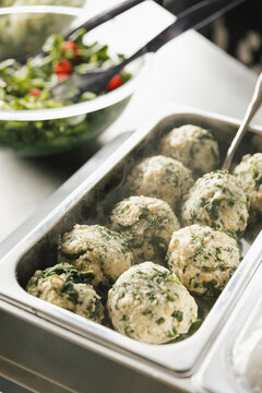Spinach bread dumplings served hot in a catering tray with a fresh salad being prepared in the background.