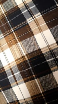 Close up of a brown, cream, and black woven fabric with a plaid pattern featuring diagonal lines and soft texture