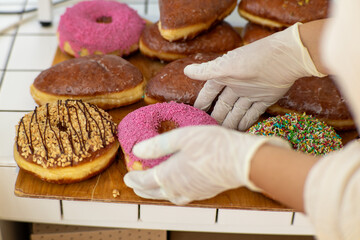 Assortment of colorful donuts on a wooden tray with gloved hands arranging them.