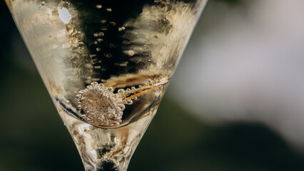 gold engagement ring with diamond lying in champagne and covered with bubbles on a black...