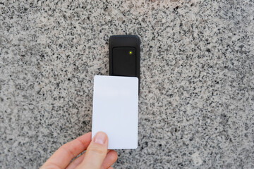 Close-up of person's hand holding a white access card near a key reader access device on granite wall. Green light indicates access granted. Security, privacy, access management, technology