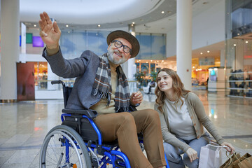 A man in a wheelchair sits beside a woman with shopping bags