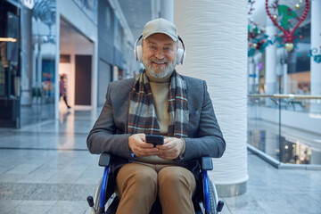 Elderly man comfortably seated in a wheelchair using his smartphone in a modern mall setting