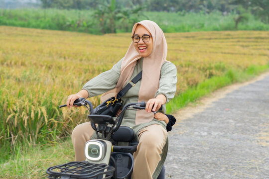 Mother and daughter ride electric bike together in rice field outdoor - Powered by Adobe