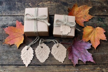 Two kraft paper gift boxes, tied with twine, adorned with autumn leaves, on a rustic wooden table