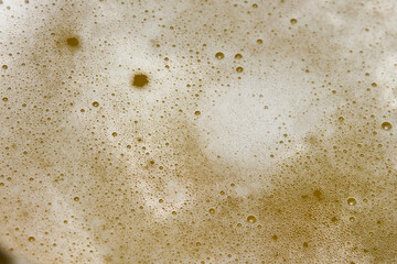 A close-up view captures rich beer foam bubbles floating atop a golden drink