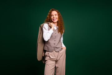 Confident young businesswoman in stylish attire posing against an emerald green background...