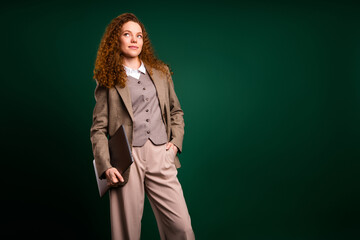 Confident red haired businesswoman wearing a formal suit against a vivid green studio background,...