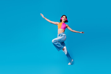Obraz premium Young woman in vibrant outfit dancing joyfully against a bright blue background, enjoying music through headphones