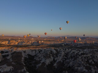 A magical drone shot of sunrise over G&ouml;reme as colorful hot air balloons lift off, painting the sky above the surreal Cappadocian landscape in golden light.