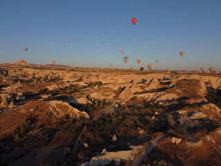 A magical drone shot of sunrise over G&ouml;reme as colorful hot air balloons lift off, painting the sky above the surreal Cappadocian landscape in golden light.