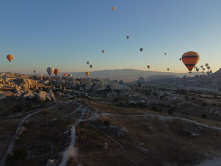 A magical drone shot of sunrise over G&ouml;reme as colorful hot air balloons lift off, painting the sky above the surreal Cappadocian landscape in golden light.