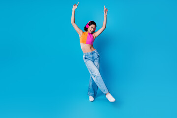 Young stylish woman dancing confidently in colorful fashion against a vibrant blue background showcasing joy and energy