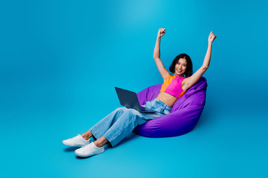 Young cheerful woman with laptop celebrating success and happiness while relaxing in a cozy bean bag chair. - Powered by Adobe