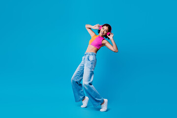 Stylish young woman dancing with headphones on vibrant blue background showcasing lifestyle, music, and colorful fashion
