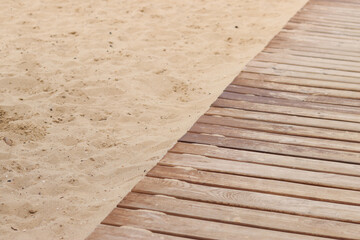Wooden decking on the beach, close-up on the boards. Boardwalk. Background. Weathered wooden boards with scattered sand, summer warm lighting. Selective focus