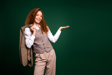 Confident young woman with red curly hair in formal attire presenting a gesture on emerald green...
