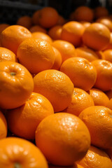 Close-up of piled oranges on a supermarket shelf under harsh, direct light, showcasing strong shadows and iridescent reflections on their surfaces