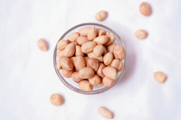 Raw peanuts spilling from a glass bowl on white background. Healthy snack and organic food concept.