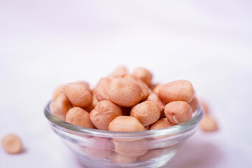 Raw peanuts spilling from a glass bowl on white background. Healthy snack and organic food concept.