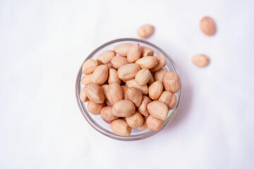 Raw peanuts spilling from a glass bowl on white background. Healthy snack and organic food concept. Copy space for advertisements.