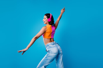 Trendy young woman dancing with headphones in casual attire against a blue background, expressing...