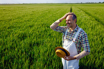 Portrait of adult male farmer standing in green wheat field.