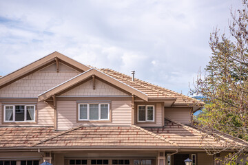 Top of grey stucco luxury house with shingle roof, green trees and nice windows in Spring in...