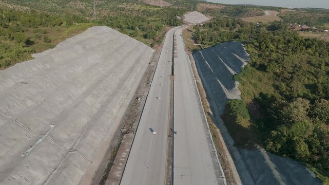 Aerial View of New Road Construction Surrounded by Lush Hills and Clear Blue Skies
