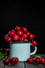 Tasty ripe red cherries in a metal blue mug on a wooden table. Fresh sweet cherry, closeup