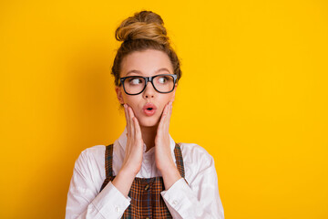 Attractive young woman expressing surprise and wonder against bright yellow background in stylish...