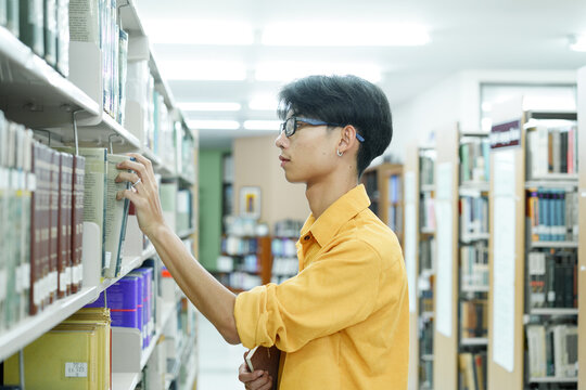 Man searching books in shelf at library. Young man taking books in a library.