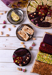 Sliced ​​Turkish delight assortment with cream filling, pistachio, almond, hazelnut, figs and cranberry laid out on plates on a white table. Local name: fistikli fitil lokum