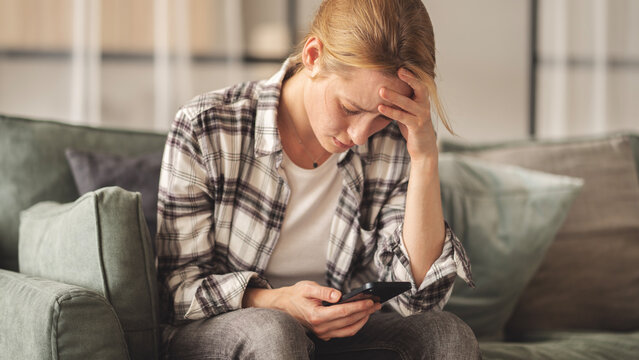 Woman reading some bad news on her smart phone, feeling sad and worried