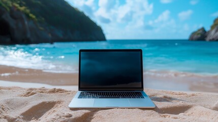 Laptop on sandy beach in front of turquoise ocean with blue sky and distant mountains. Concept of digital nomad lifestyle