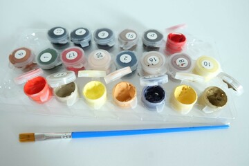 Watercolor paint set, a used paint palette with brushes placed beside it, each color contained in a...