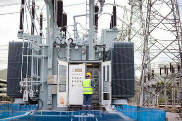 Engineer performs inspection on large transformer at electrical substation ensuring safety and...