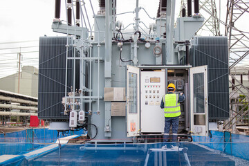 Engineer performs inspection on large transformer at outdoor substation ensuring safety and...