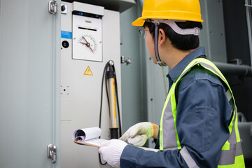 Engineer wearing yellow helmet performs inspection on transformer inside substation with focused...