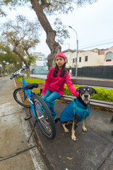 A girl is sitting on a bicycle with a dog on her lap