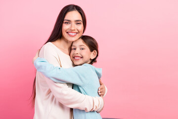 Loving mother embracing her happy daughter in a warm hug against a bright pink background,...