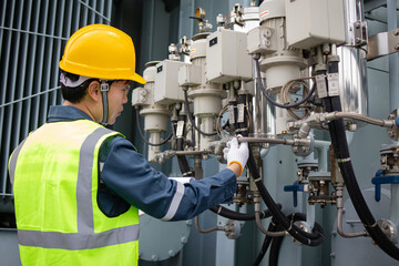 Technician wearing yellow helmet and reflective vest inspects oil filter valve at electrical...