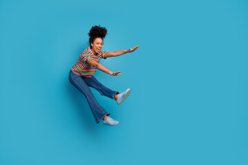 Young stylish woman in a vibrant striped t-shirt jumping energetically against a turquoise...