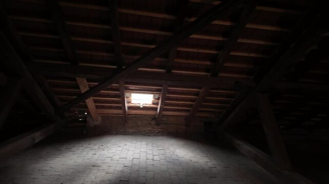 View of an empty attic with an illuminated dormer window in an old house. Abandoned attic in an ancient building. Concept of old times and romanticism