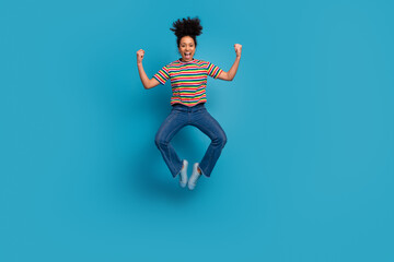Happy young woman in striped shirt celebrates with joyful jump against bright teal background