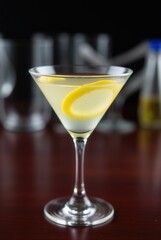 Lemon Twist Martini: A classic martini cocktail garnished with a lemon twist, sitting on a dark wood surface. The background shows other glassware. 